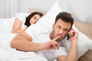 man talking in bed on mobile next to his girlfriend